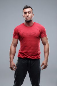 Portrait of a young serious man in red t-shirt over gray background