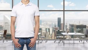 A man in a white polo shirt and denims holds his hands in pockets. A modern panoramic office space in New York City. Manhattan panoramic view.